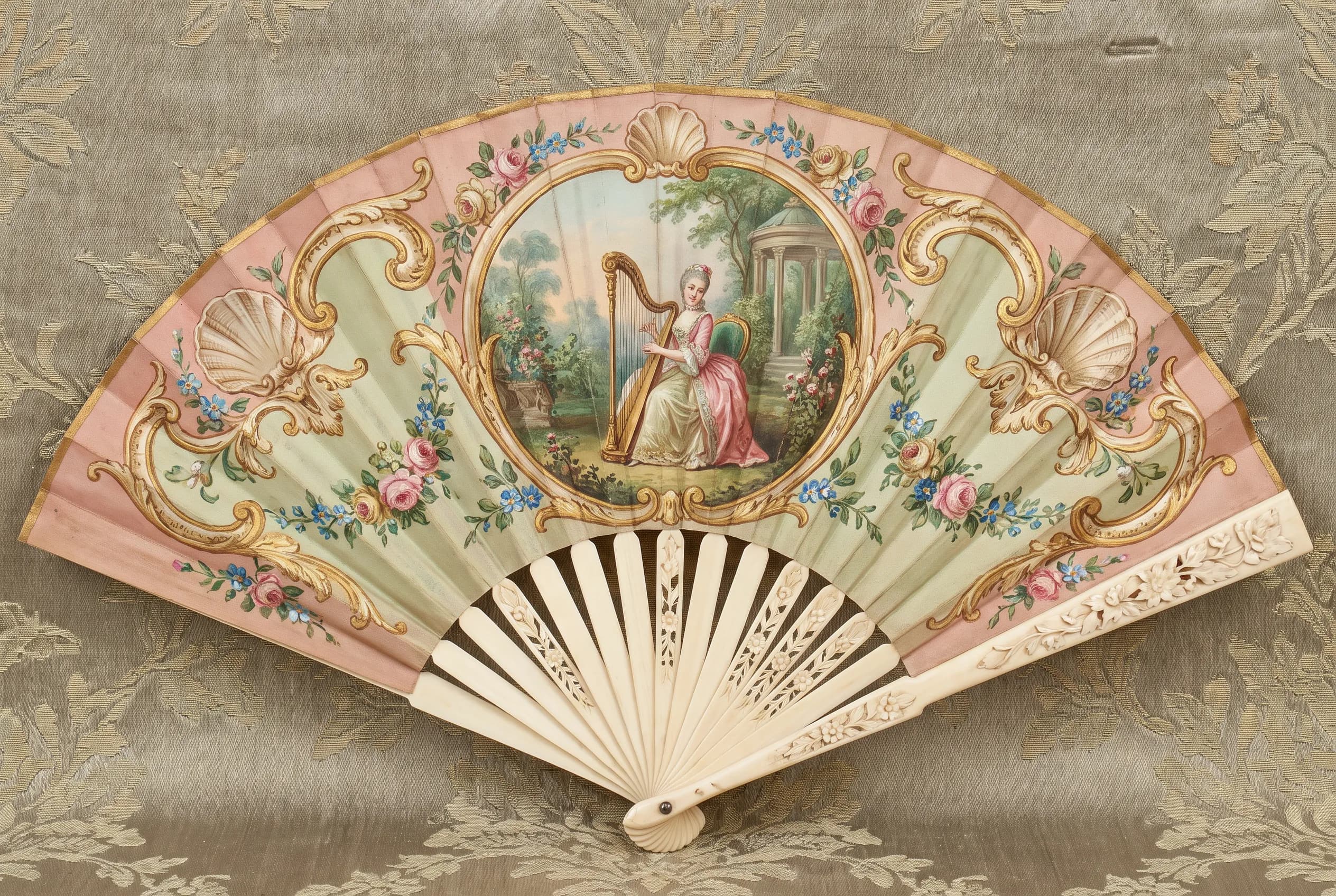 Painted silk fan showing a harpist in a garden framed by gilt scrolls, rococo art style