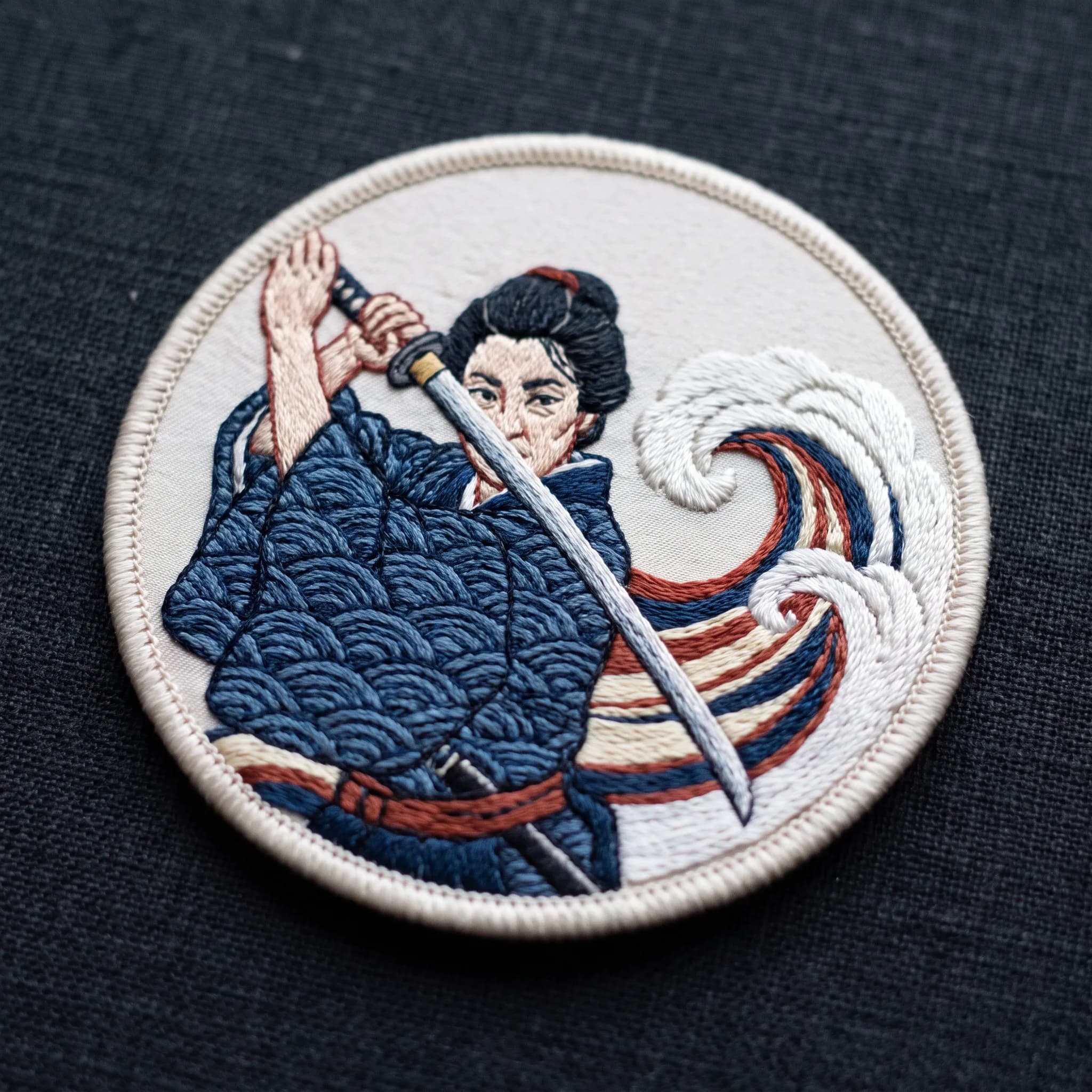 Embroidered silk patch of a swordswoman in her forties with a stitched curl of water, Demon Slayer art style