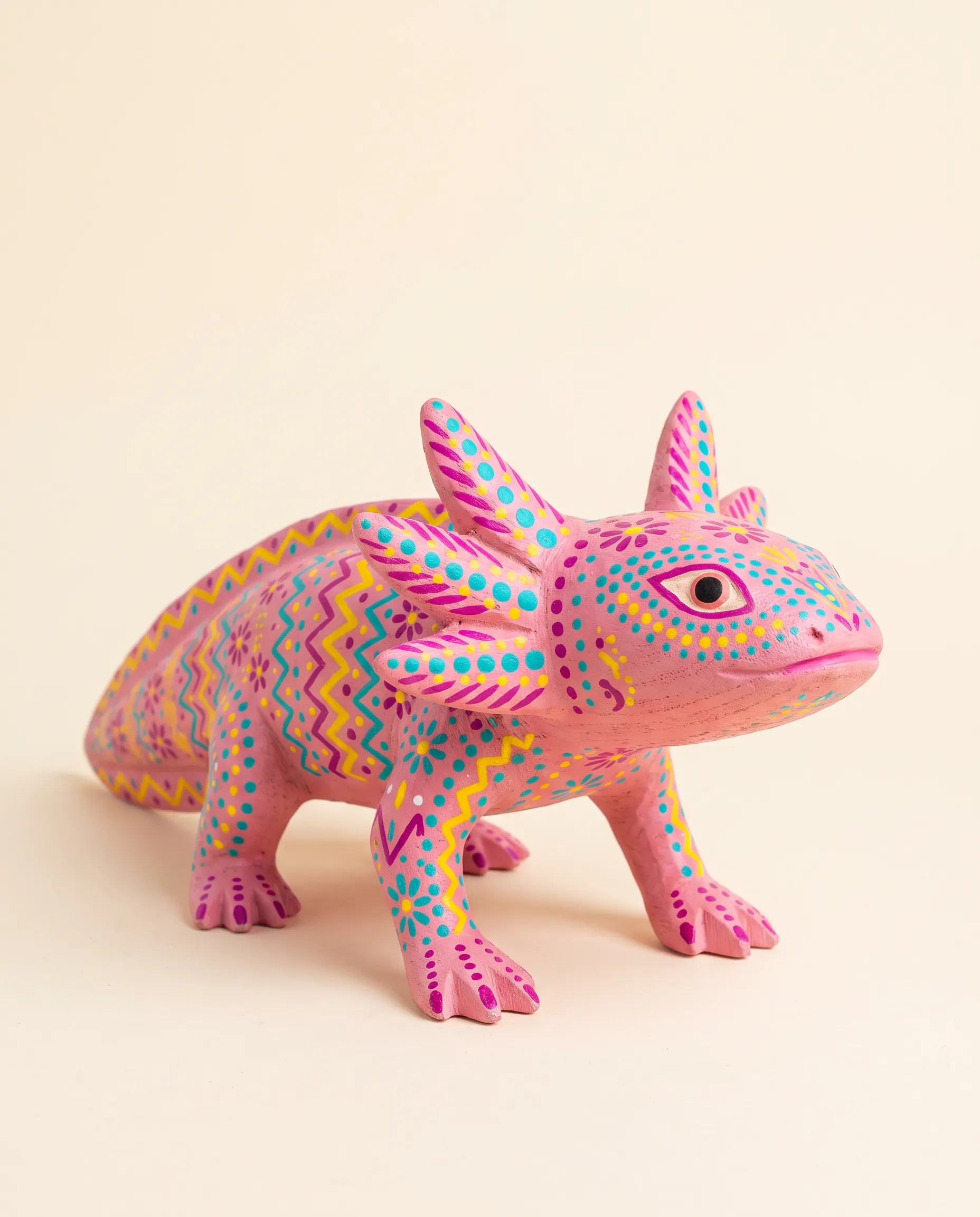 Painted Oaxacan copal wood carving of a pink axolotl covered in dots and zigzags, Mexican folk art style