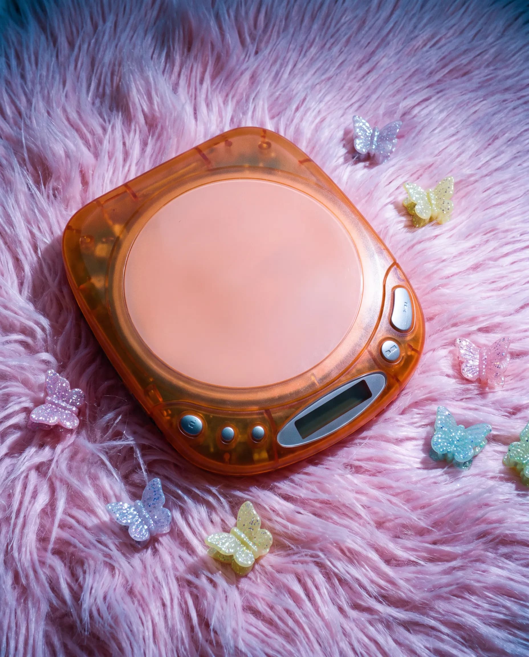 Flash photograph of a translucent tangerine portable CD player on pink faux fur, Y2K art style