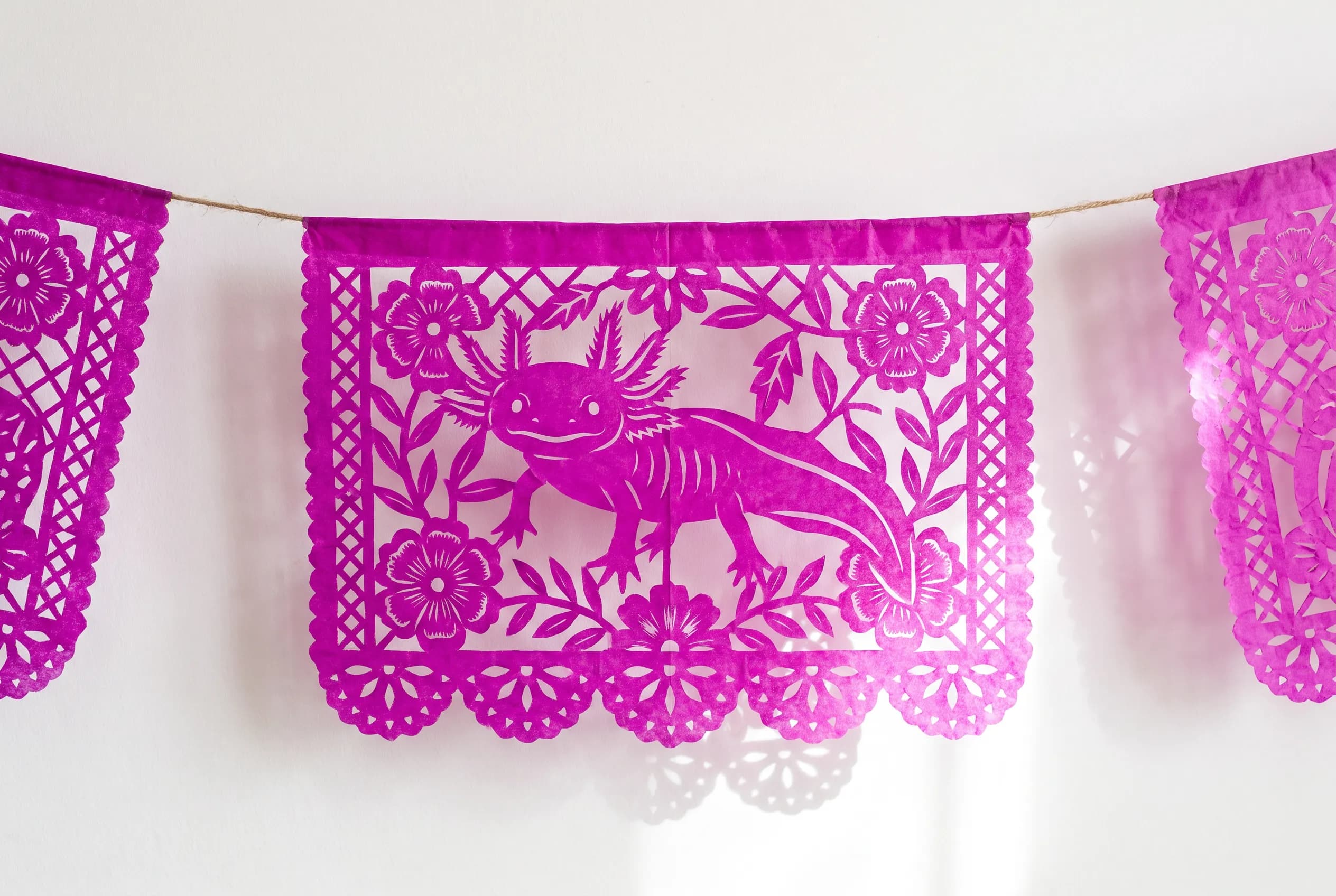 Magenta papel picado banner with an axolotl cut among marigolds, Mexican folk art style
