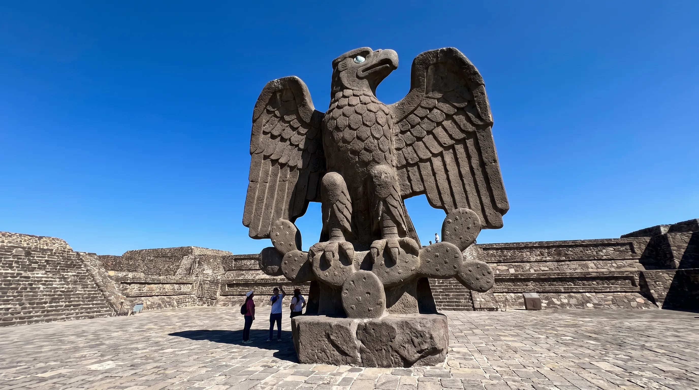 Monumental basalt eagle with spread wings atop a nopal cactus in a sunlit plaza, Aztec art style