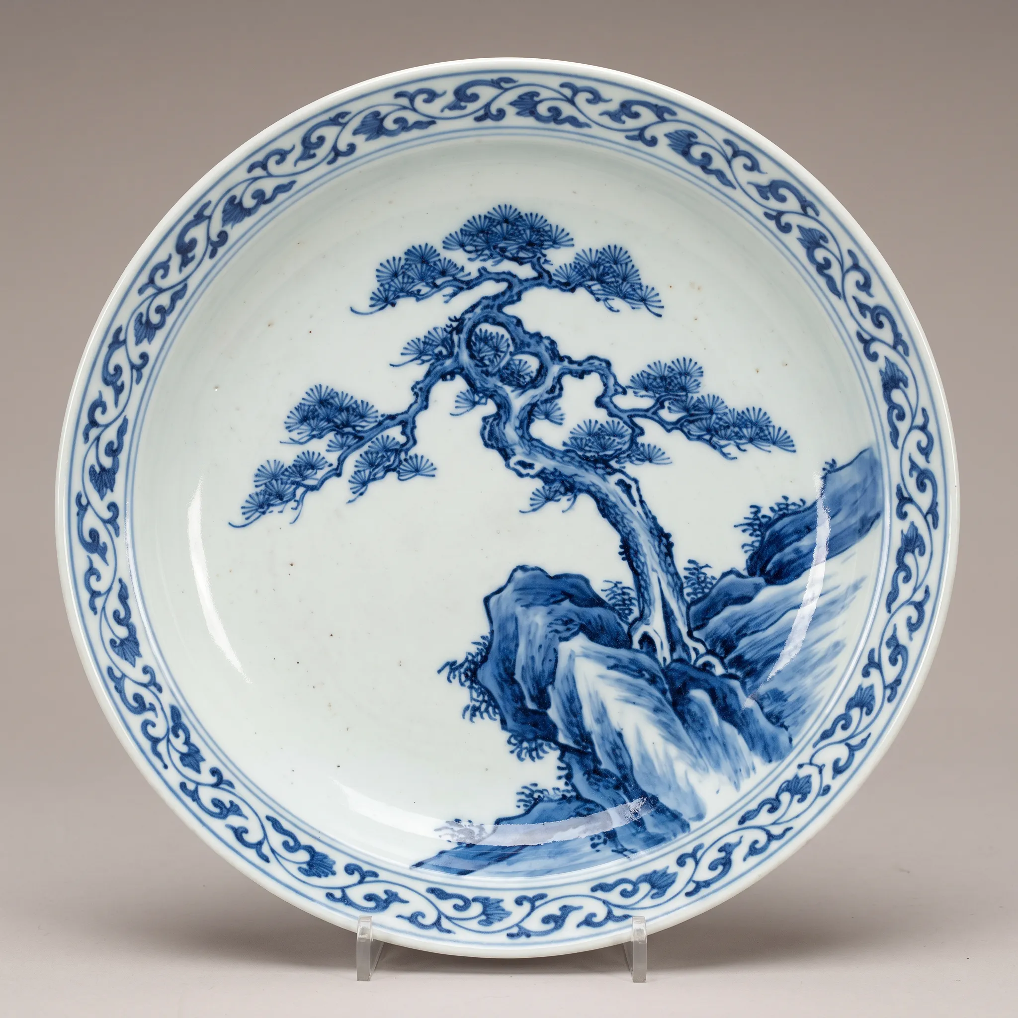 Porcelain plate painted in cobalt blue with a windswept pine growing from rocks, blue-and-white Chinese art style
