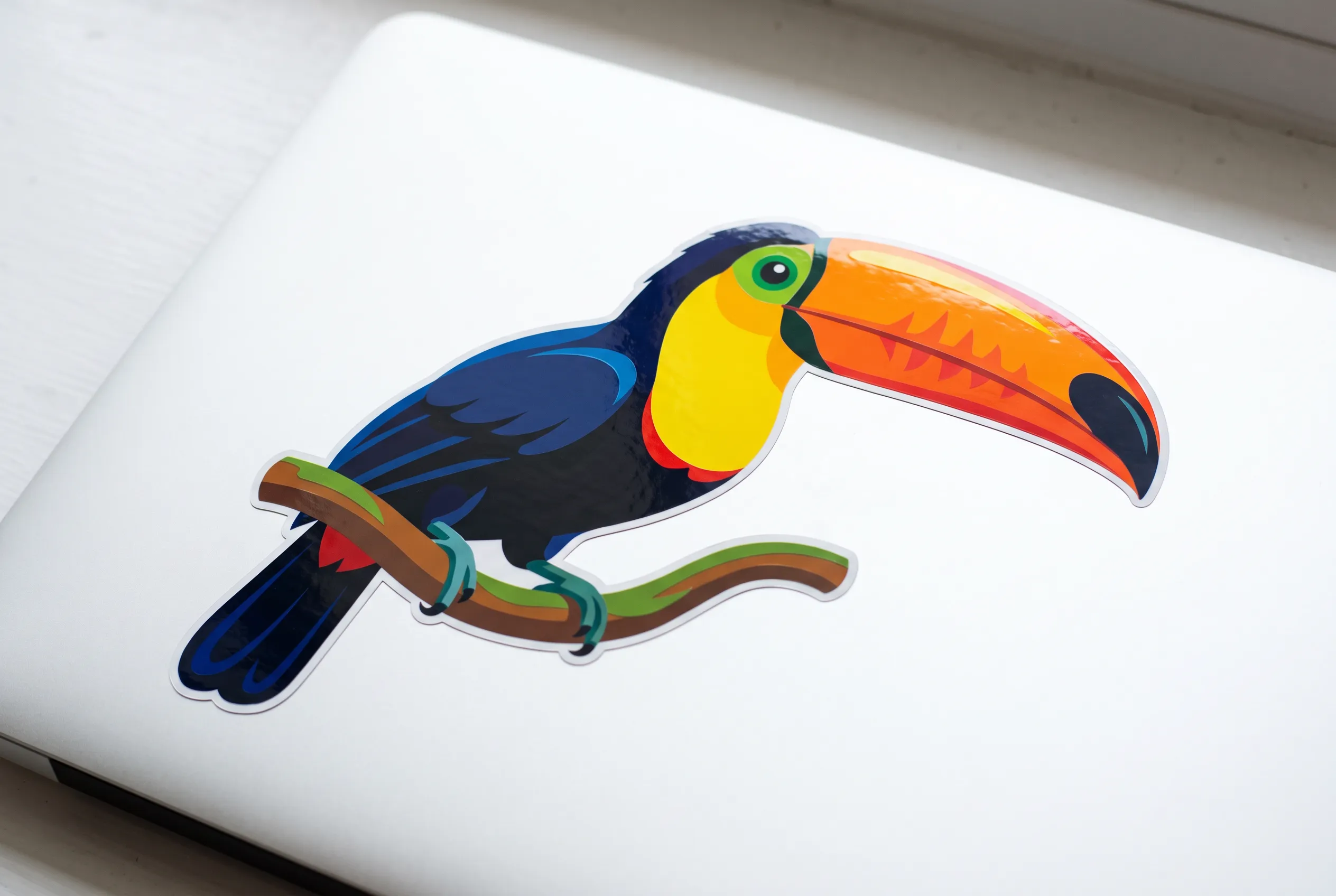 Die-cut vinyl decal of a toucan on a white laptop lid, vector art style