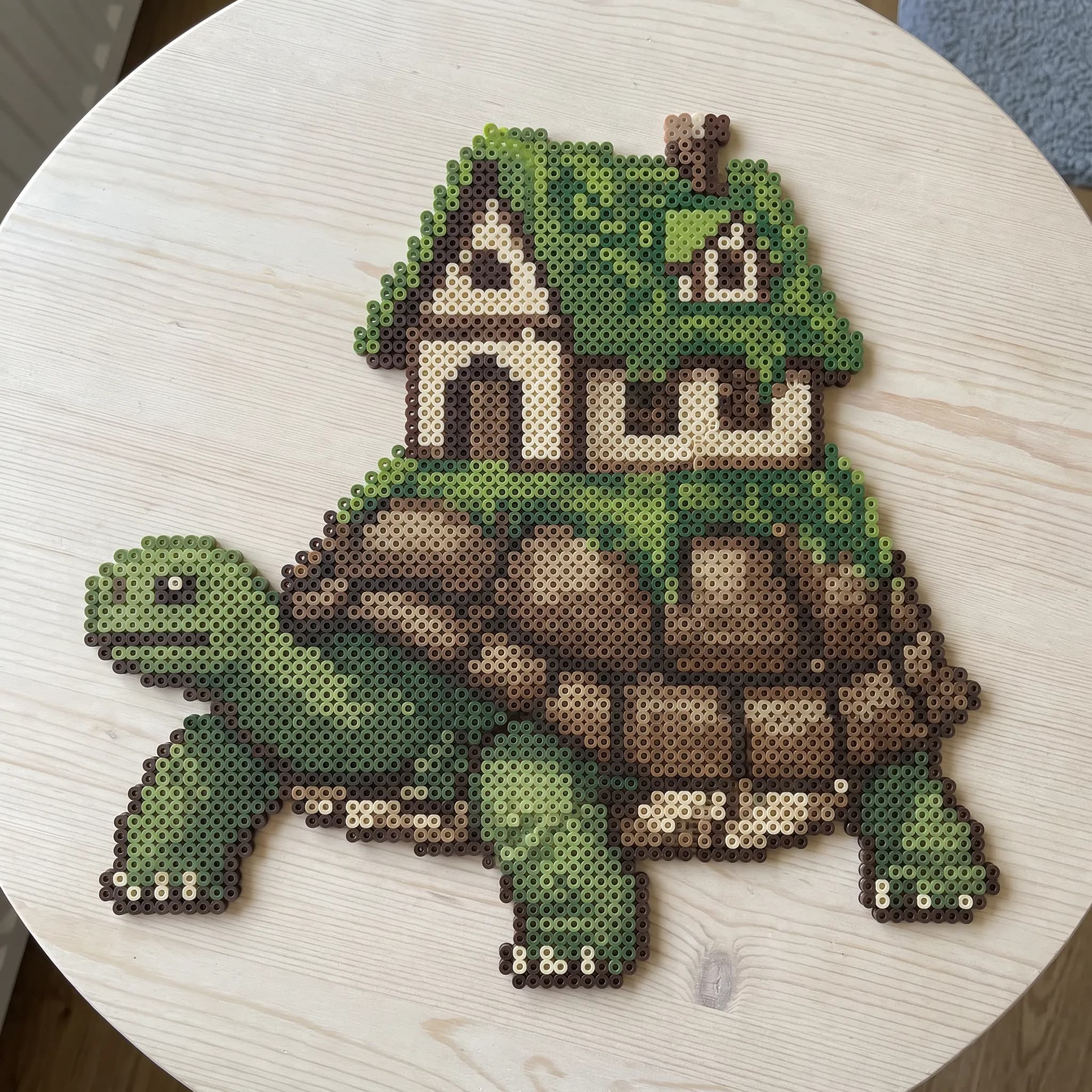 Giant tortoise carrying a moss-roofed cottage, pixel art made from ironed fuse beads