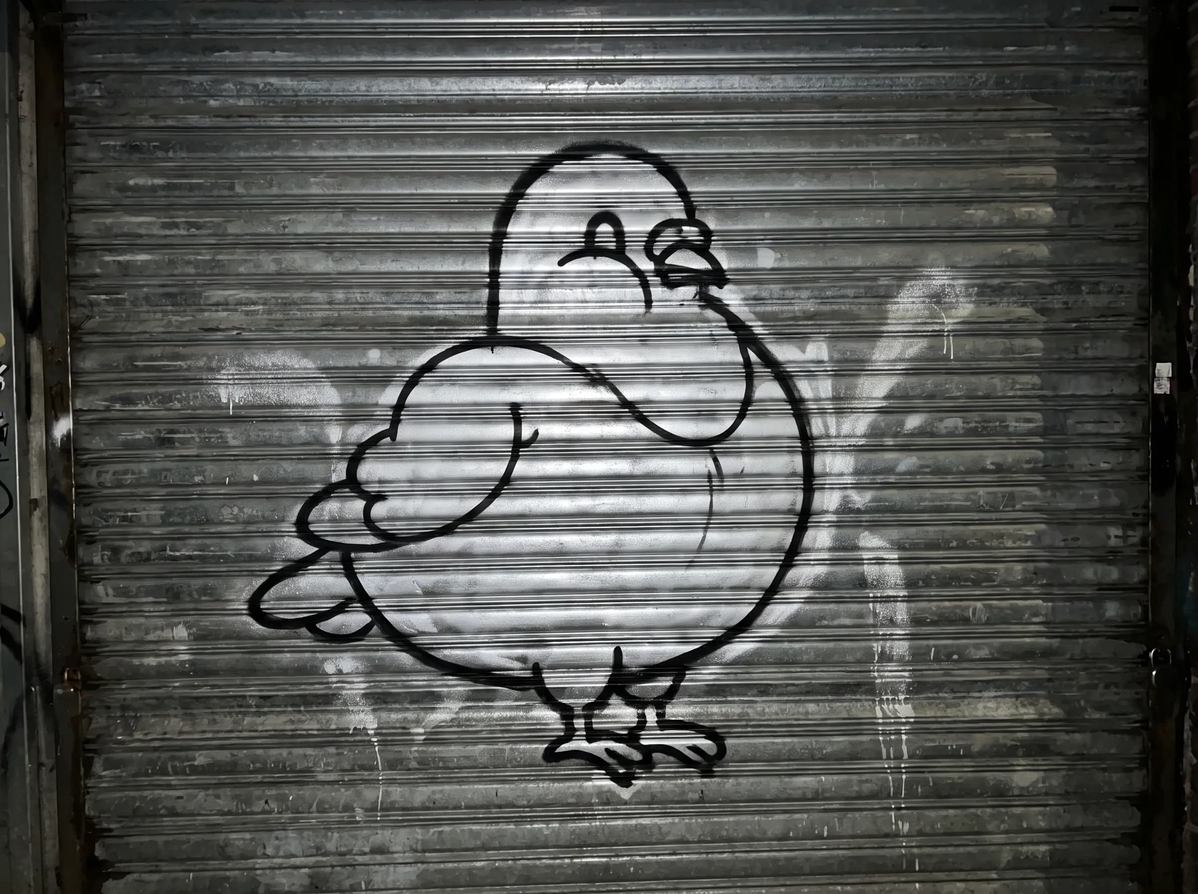 Plump city pigeon painted as a silver and black throw-up on a shop shutter, throw-up graffiti style