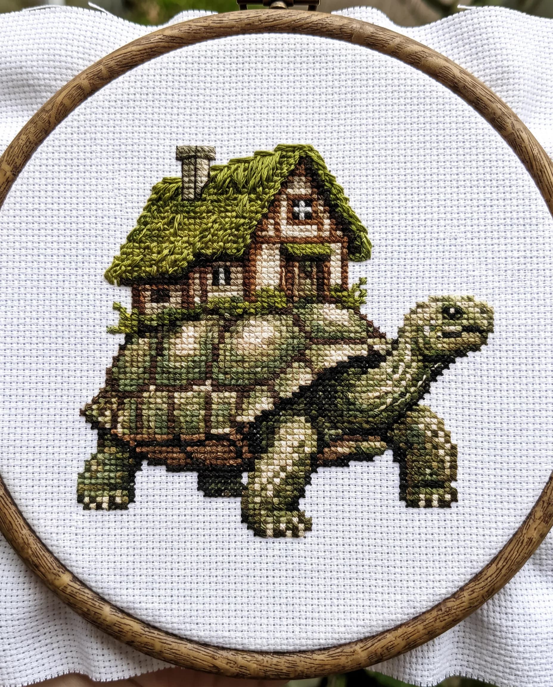 Giant tortoise carrying a moss-roofed cottage, pixel art stitched in cross-stitch embroidery